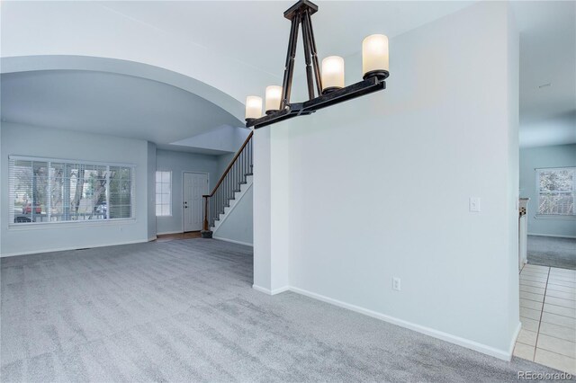 unfurnished living room featuring baseboards, arched walkways, carpet, and stairway
