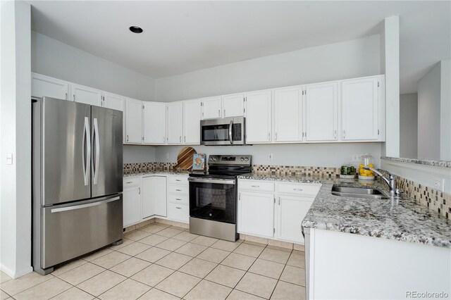 kitchen with white cabinets, light stone countertops, a sink, stainless steel appliances, and light tile patterned floors
