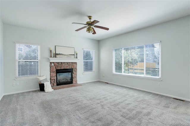 unfurnished living room with baseboards, a stone fireplace, ceiling fan, and carpet
