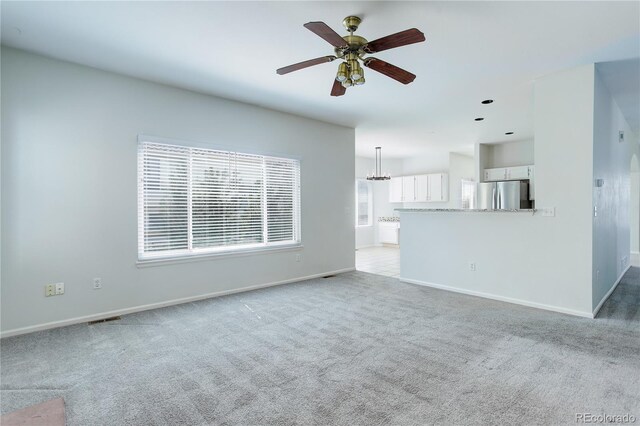 unfurnished living room with carpet floors, baseboards, ceiling fan with notable chandelier, and visible vents