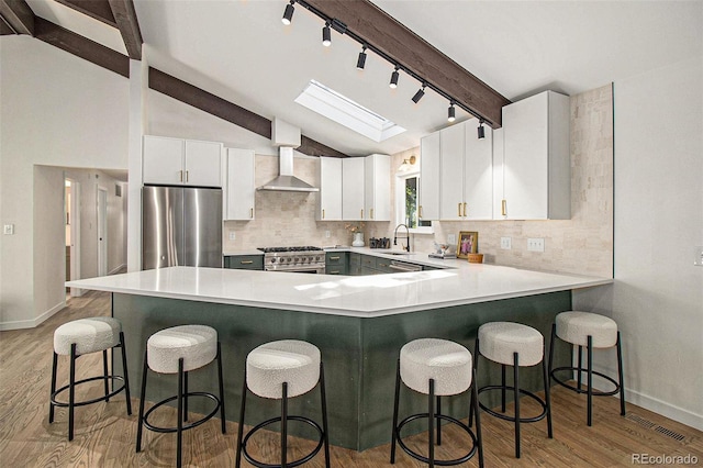 14890 W 58th Pl, Golden, CO 80403 - kitchen featuring stainless steel appliances, track lighting, wall chimney range hood, light wood-style floors, and decorative backsplash