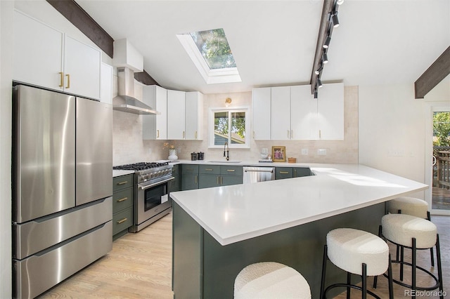 14890 W 58th Pl, Golden, CO 80403 - kitchen with stainless steel appliances, wall chimney range hood, a kitchen bar, a skylight, and vaulted ceiling
