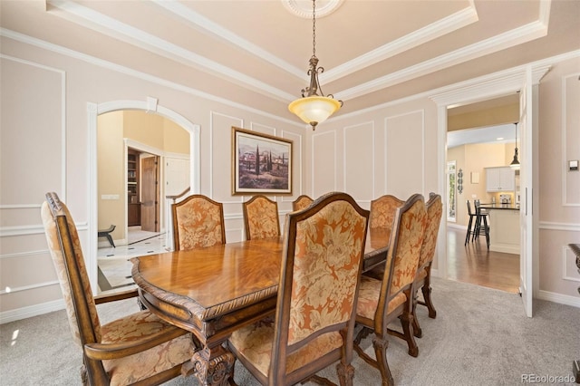 carpeted dining area with crown molding and a raised ceiling