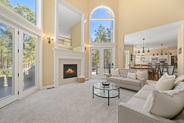 living room featuring a high ceiling, a brick fireplace, light carpet, and french doors