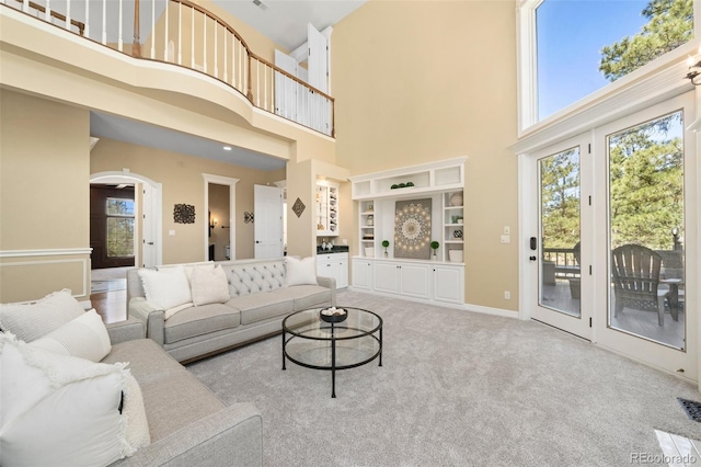 living room with a towering ceiling, light carpet, and built in shelves