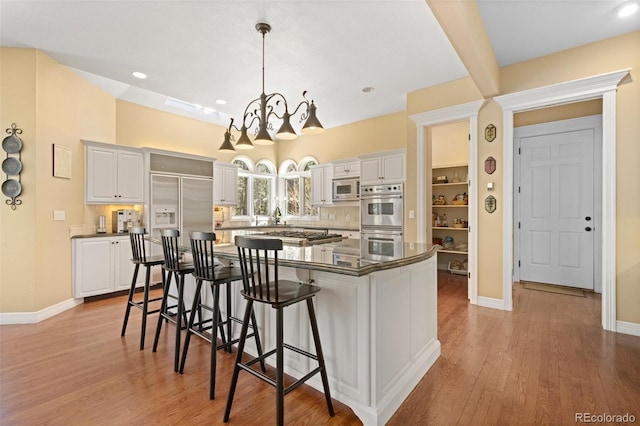 kitchen featuring a kitchen island, decorative light fixtures, white cabinets, stainless steel appliances, and light hardwood / wood-style flooring