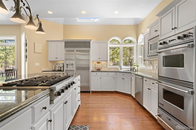 kitchen with white cabinetry, built in appliances, and pendant lighting