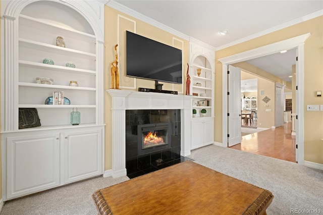 living room featuring built in shelves, ornamental molding, a tile fireplace, and light carpet