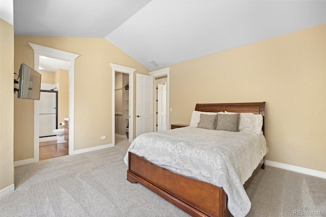 bedroom with a walk in closet, vaulted ceiling, carpet, and ensuite bathroom