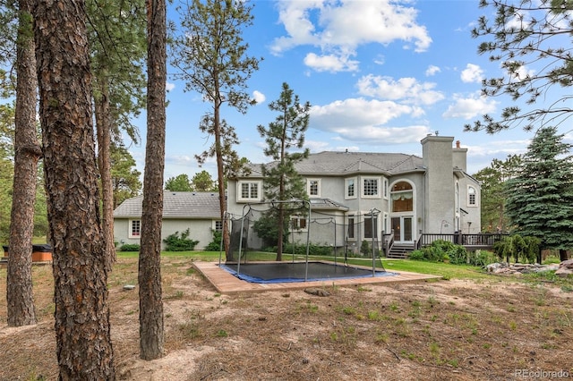 rear view of property with a wooden deck, a trampoline, and a lawn