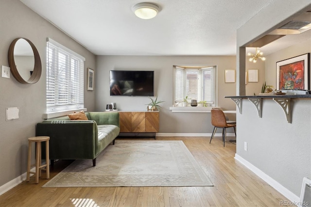 living room with an inviting chandelier, baseboards, light wood-type flooring, and a textured ceiling