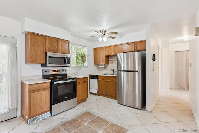 kitchen with stainless steel appliances, a sink, light countertops, a ceiling fan, and brown cabinets