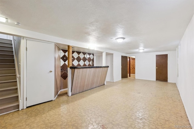 finished basement featuring stairway, light floors, a textured ceiling, and baseboards