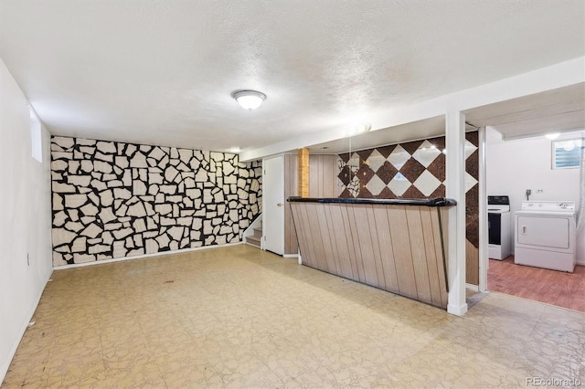 finished basement with washer and dryer, tile patterned floors, a textured ceiling, and a bar