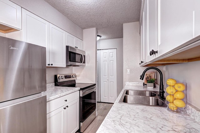 kitchen with sink, light hardwood / wood-style flooring, a textured ceiling, white cabinetry, and stainless steel appliances