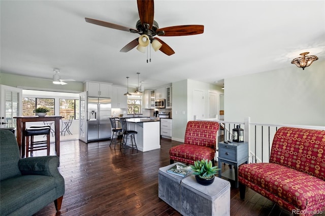 living room with a ceiling fan, baseboards, and dark wood-style floors