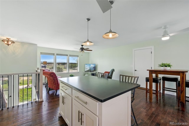 kitchen with dark countertops, dark wood finished floors, a center island, a ceiling fan, and pendant lighting