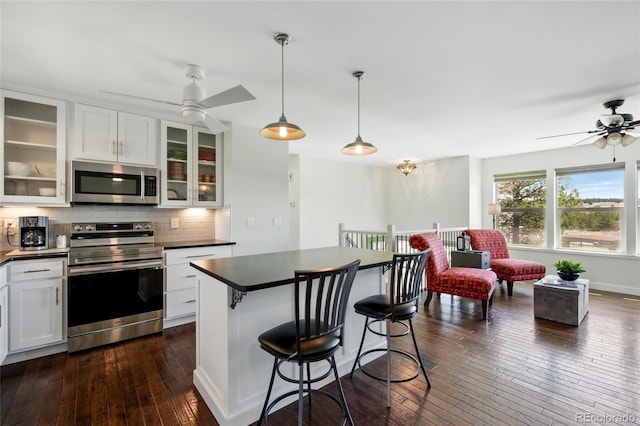 kitchen featuring ceiling fan, backsplash, dark wood-style flooring, dark countertops, and stainless steel appliances