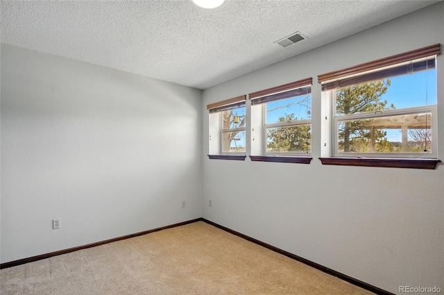 spare room with baseboards, visible vents, a textured ceiling, and light colored carpet