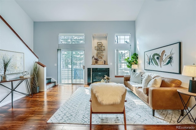 living area with stairway, a healthy amount of sunlight, wood finished floors, and a towering ceiling