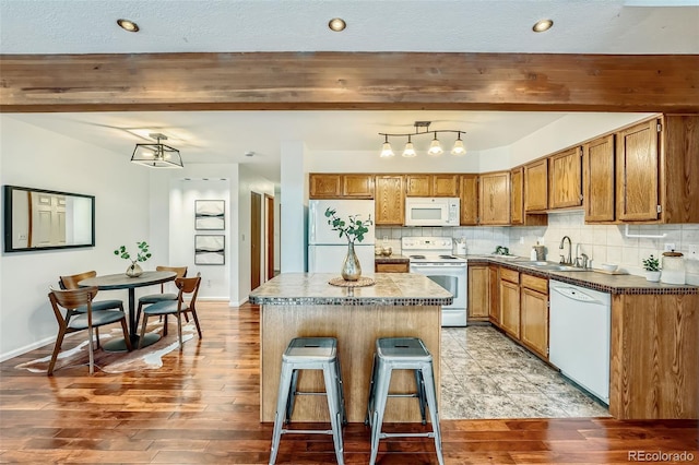 kitchen featuring beam ceiling, backsplash, white appliances, and a center island