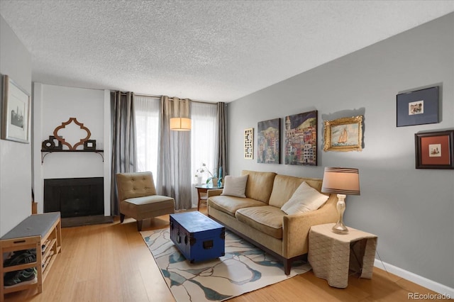 living area with a fireplace with raised hearth, a textured ceiling, baseboards, and wood finished floors