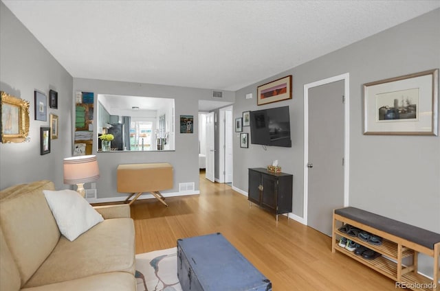 living room featuring a textured ceiling, wood finished floors, visible vents, and baseboards