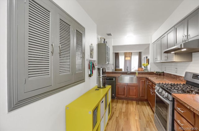 kitchen with light wood-style floors, dishwasher, under cabinet range hood, a sink, and gas stove