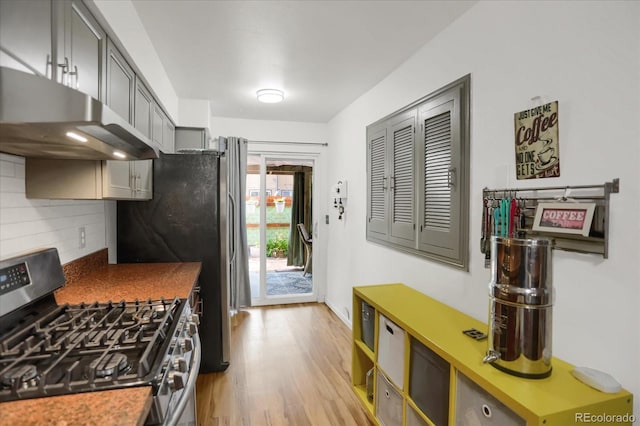 kitchen with stainless steel appliances, light wood-type flooring, under cabinet range hood, and tasteful backsplash