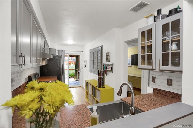 kitchen with visible vents, backsplash, stove, glass insert cabinets, and a sink