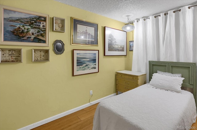 bedroom featuring a textured ceiling, wood finished floors, and baseboards