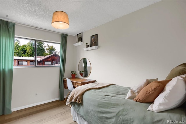 bedroom with a textured ceiling, baseboards, and wood finished floors