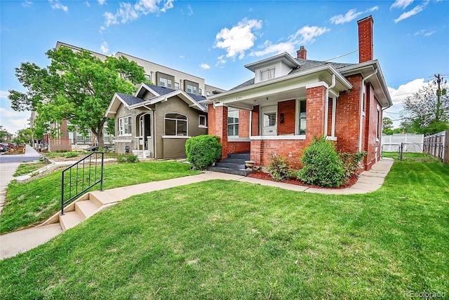 bungalow-style home featuring fence, covered porch, a front yard, a chimney, and brick siding