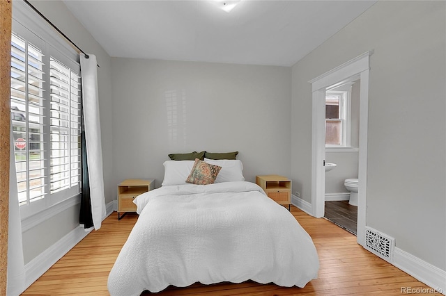 bedroom featuring visible vents, baseboards, light wood finished floors, and ensuite bathroom