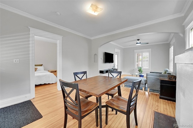 dining area with arched walkways, light wood finished floors, a ceiling fan, and ornamental molding