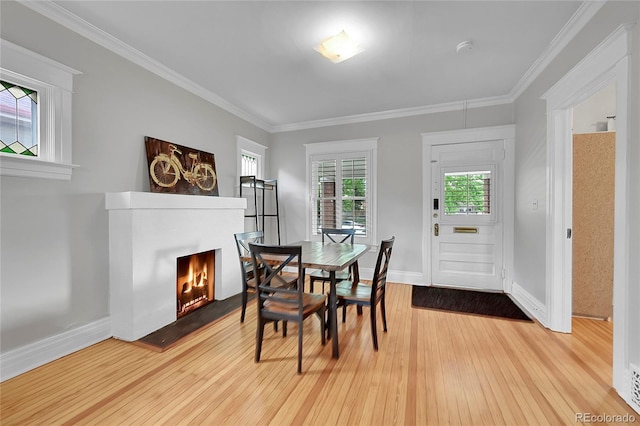 dining area featuring baseboards, ornamental molding, a lit fireplace, and hardwood / wood-style floors