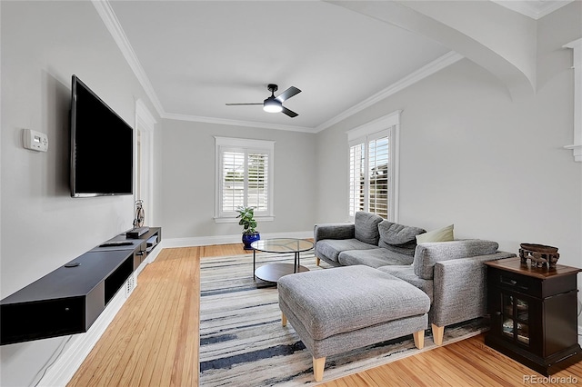 living area with a ceiling fan, arched walkways, wood finished floors, baseboards, and ornamental molding