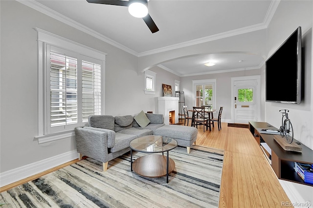 living area with ceiling fan, arched walkways, baseboards, wood finished floors, and ornamental molding