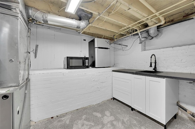 unfinished basement featuring a sink, heating unit, and freestanding refrigerator