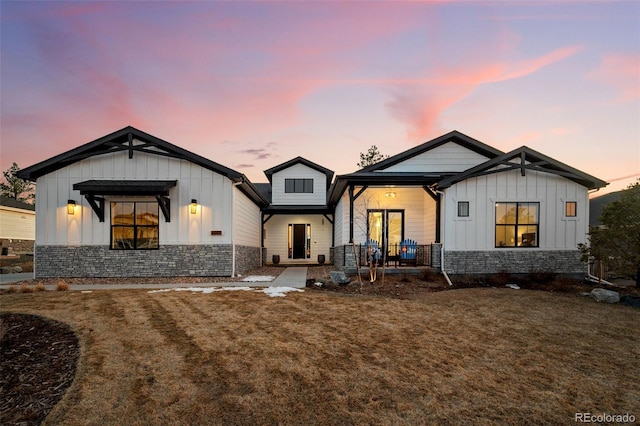 view of front of house featuring a front yard, covered porch, board and batten siding, and stone siding