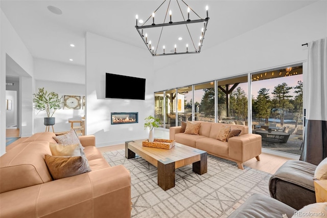 living area with baseboards, a high ceiling, recessed lighting, light wood-style floors, and a glass covered fireplace