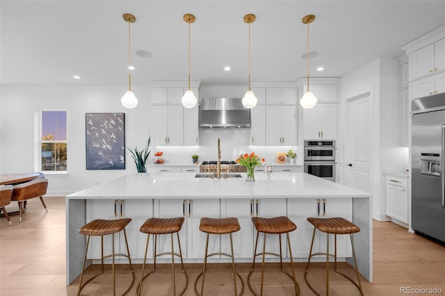 kitchen with stainless steel appliances, light wood-style flooring, white cabinets, and wall chimney range hood