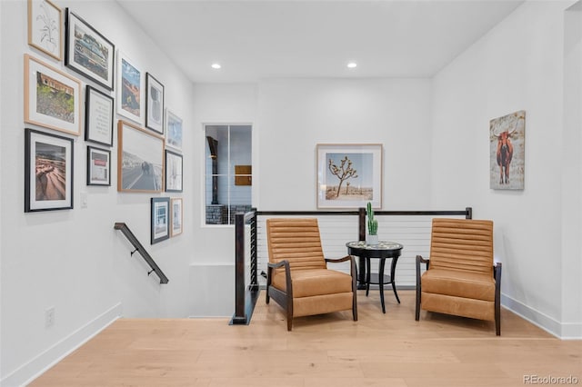 sitting room with an upstairs landing, recessed lighting, baseboards, and wood finished floors