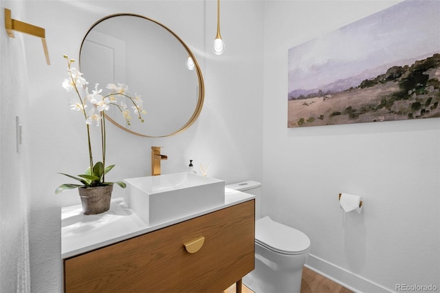 bathroom featuring baseboards, toilet, wood finished floors, and vanity