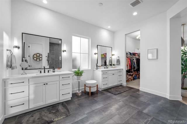 full bath featuring visible vents, two vanities, baseboards, and a sink