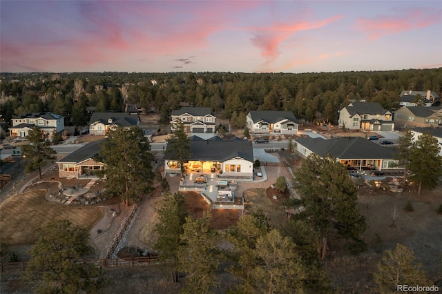 aerial view at dusk featuring a forest view and a residential view