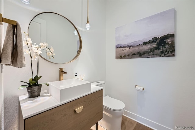 half bath with baseboards, wood finished floors, toilet, and vanity