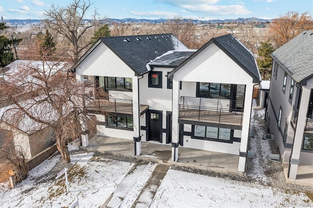 snow covered property featuring a balcony, stucco siding, a patio area, and a mountain view