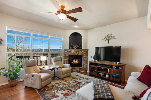 living area featuring a fireplace, baseboards, ceiling fan, and wood finished floors