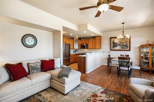 living room with recessed lighting, ceiling fan with notable chandelier, baseboards, and light wood-style floors